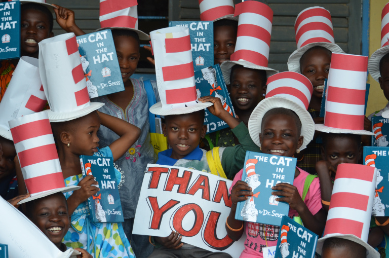 a group of children holding copies of the cat in the hat books and wearing red and white hats